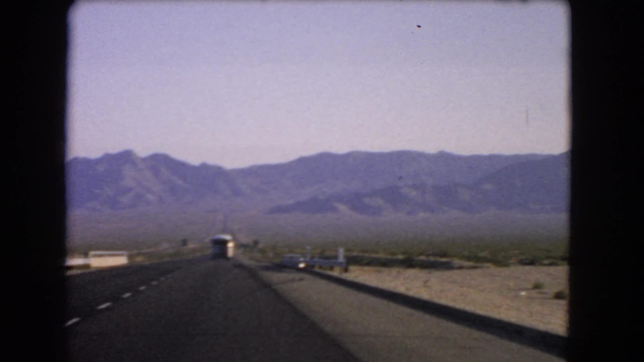Desert highway leading toward mountains with a white bus ahead.
