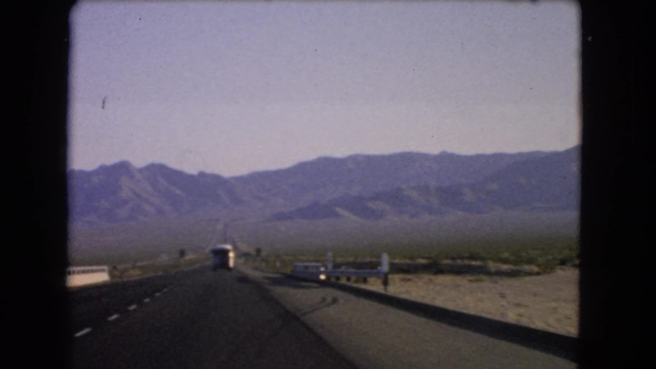 1966 Nevada 8mm frame showing a car-passenger view along a highway with a bus ahead and mountains across the desert horizon.