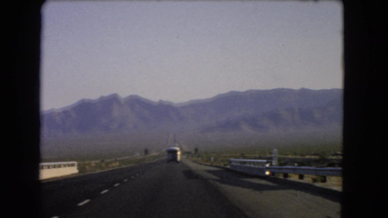 Highway seen from a moving car with a white bus ahead and mountains in the distance.