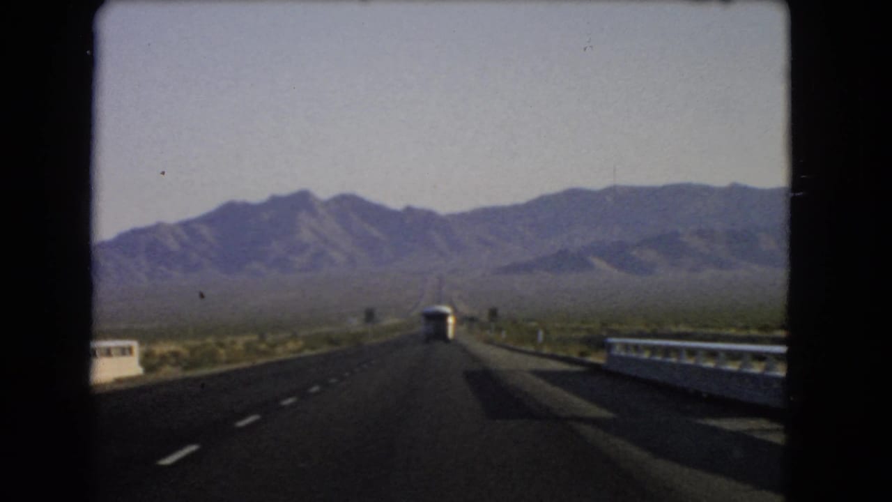 Roadway and guardrails stretch toward mountains with a white bus centered ahead.