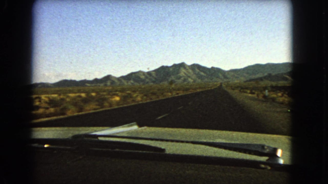 1966 Nevada 8mm passenger view over a car hood and windshield wiper toward an empty desert highway and distant mountains.