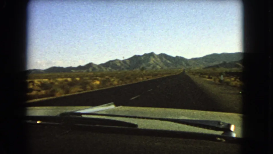 1966 Nevada 8mm passenger view over a car hood and windshield wiper toward an empty desert highway and distant mountains.