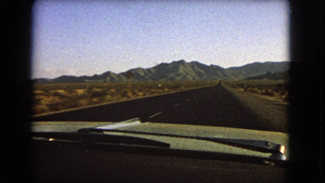 Car-dashboard view of a desert road running toward low mountains under a clear sky.