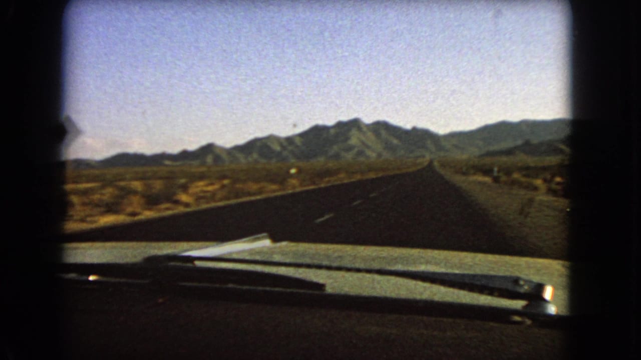 Passenger-seat 8mm frame from Nevada in 1966, with the car hood at bottom and a straight road crossing an arid plain.