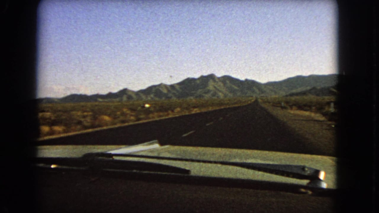 1966 8mm Nevada road view over a car hood, with windshield wipers, desert terrain, and distant mountains under a clear sky.