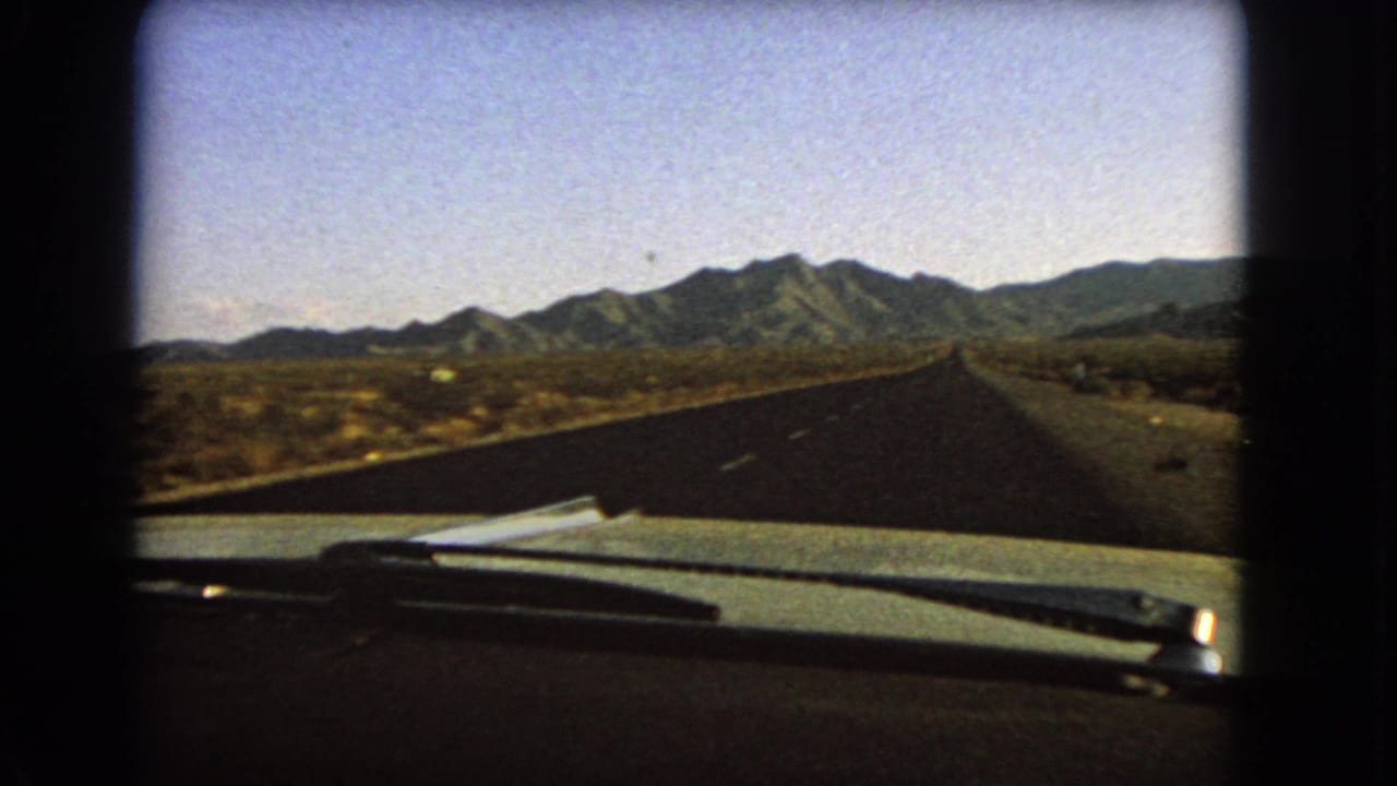 Straight desert road extending toward mountains beyond the car windshield.