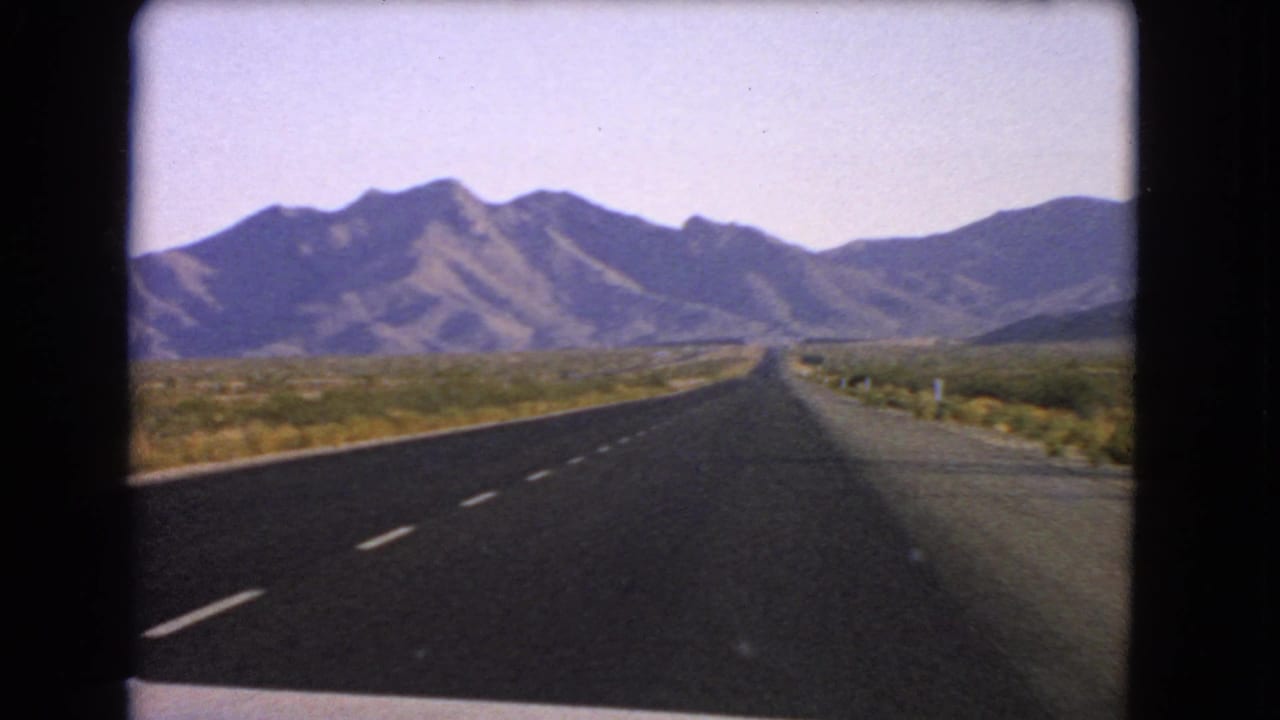 Paved highway receding into desert hills with roadside posts visible.