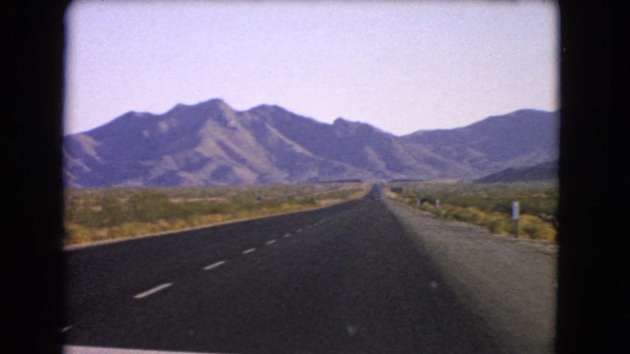 Final 1966 Nevada road frame showing the highway, roadside shoulder, desert scrub, and distant hills in soft 8mm color.