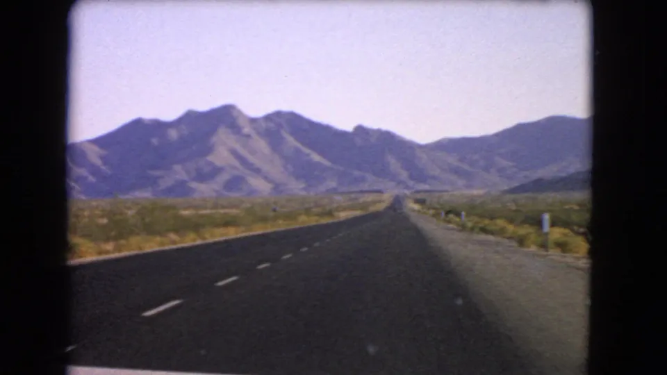 Final 1966 Nevada road frame showing the highway, roadside shoulder, desert scrub, and distant hills in soft 8mm color.