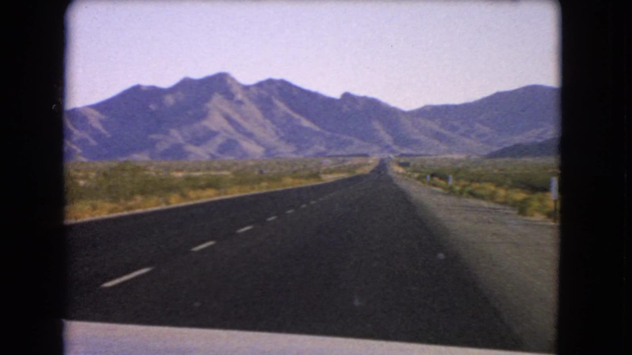 1966 Nevada 8mm road view from a moving car, with an open highway stretching toward rugged mountains.