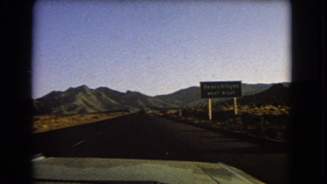 Close 1966 8mm frame of a roadside sign reading Searchlight next right along a Nevada desert highway.