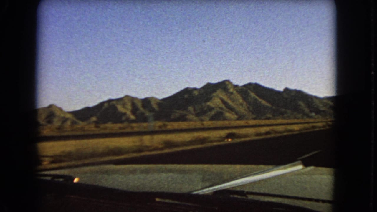 Passenger-side road view with dry terrain, mountains, and part of the vehicle visible.