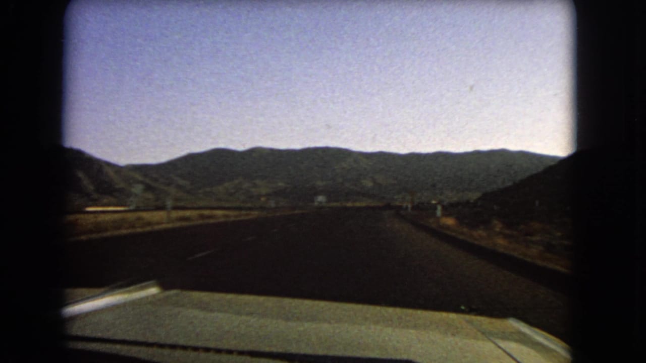 In-car 8mm view of a Nevada highway continuing toward mountain ridges under a pale sky in 1966.