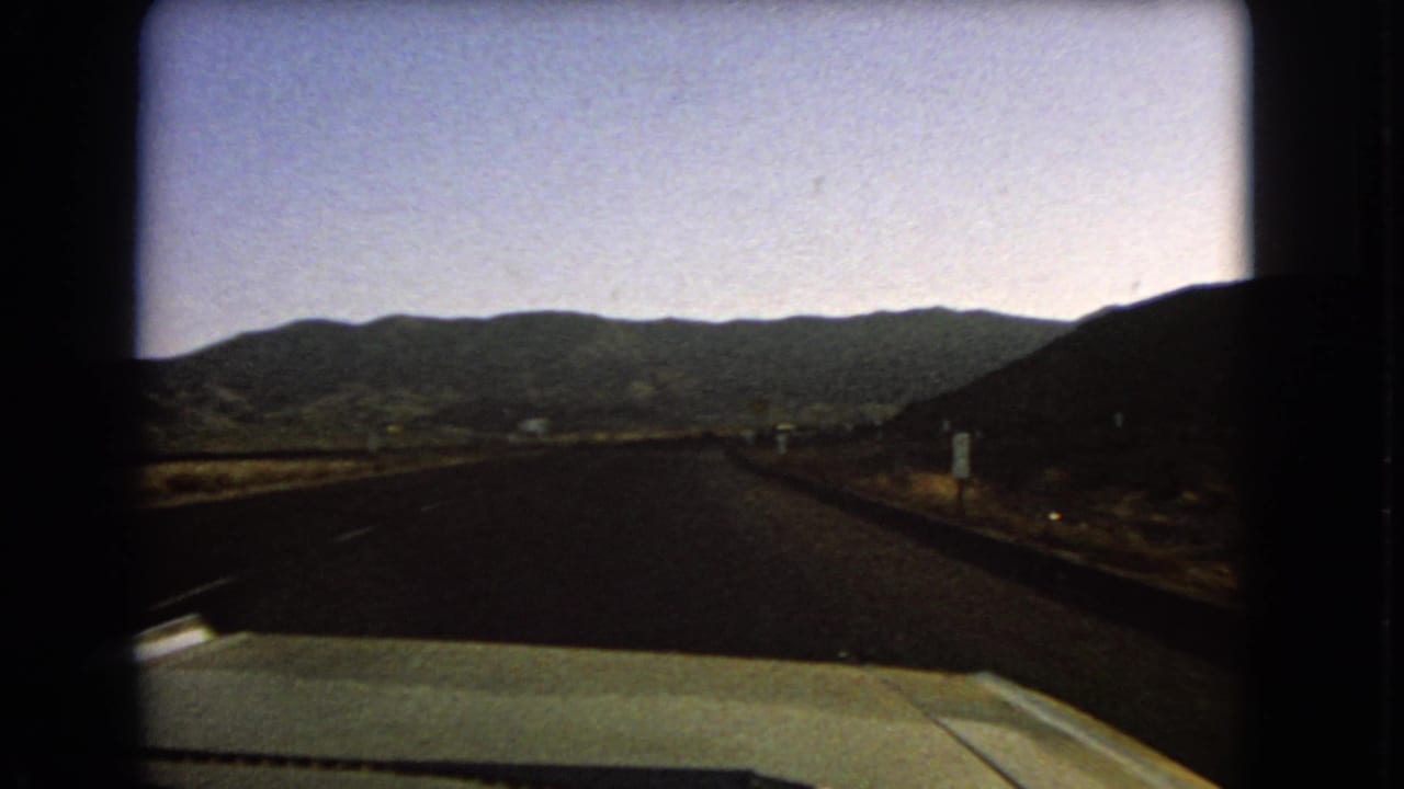1966 Nevada road footage from a moving car, with a straight highway, arid roadside, and mountains ahead.