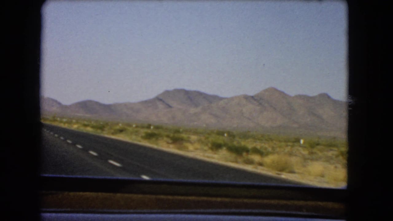 Nevada 8mm travel frame showing a highway shoulder, arid roadside plants, and mountains across the horizon.