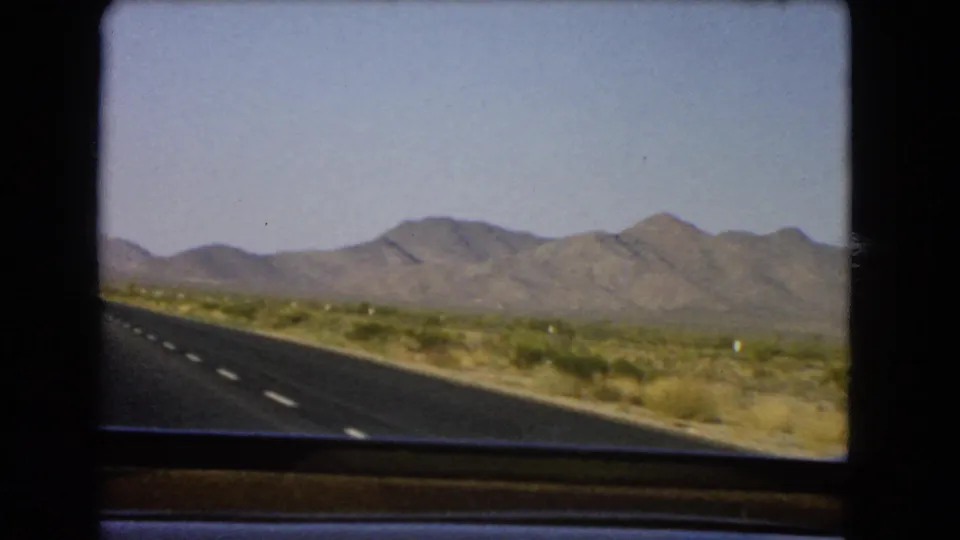 Nevada 8mm travel frame showing a highway shoulder, arid roadside plants, and mountains across the horizon.