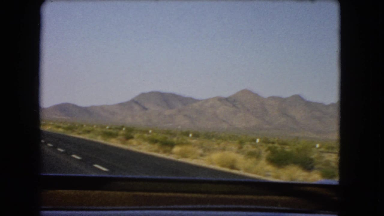Paved desert highway seen from inside a moving car with mountains ahead.