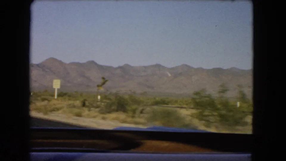 1966 Nevada desert highway footage showing low vegetation, roadside markers, and mountains seen from inside a moving vehicle.