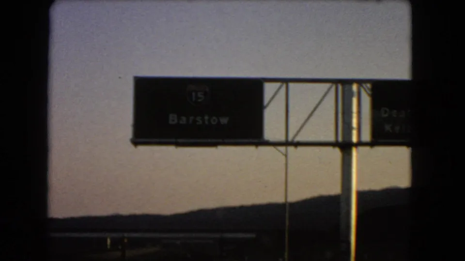 1966 road footage showing an overhead Interstate 15 sign for Barstow against desert hills and sky.
