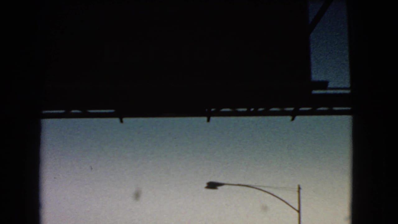 A passing 8mm travel frame with heavy dark framing, twilight sky, and a roadside streetlight or utility pole.