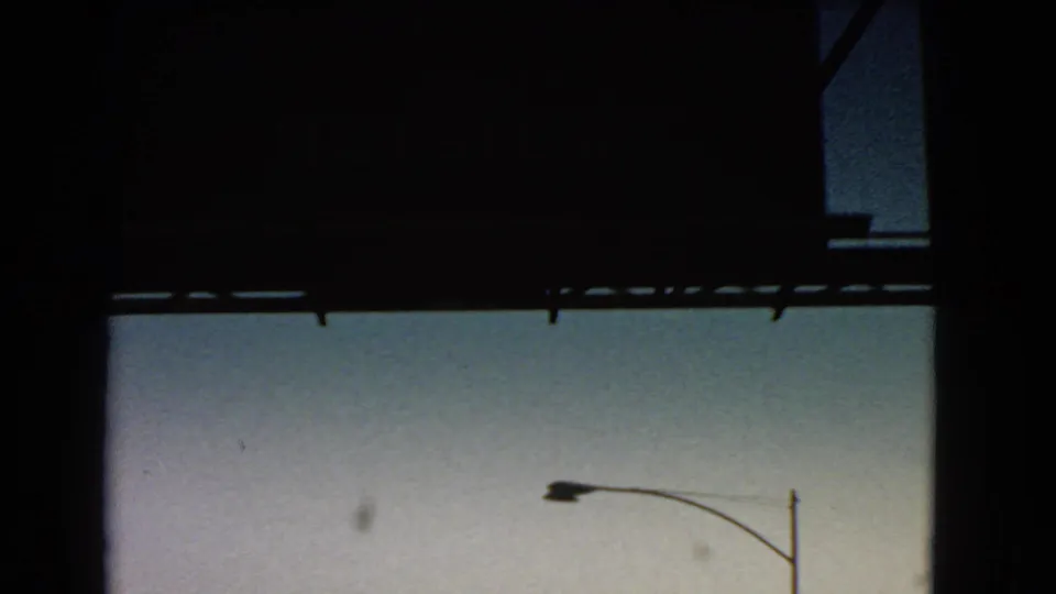 A passing 8mm travel frame with heavy dark framing, twilight sky, and a roadside streetlight or utility pole.