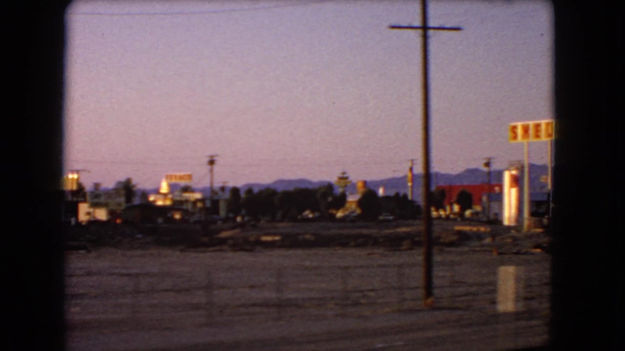 A later 8mm frame shows Shell signage, a tall utility pole, small roadside buildings, and desert mountains at dusk.