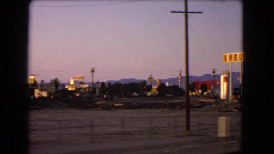 A later 8mm frame shows Shell signage, a tall utility pole, small roadside buildings, and desert mountains at dusk.