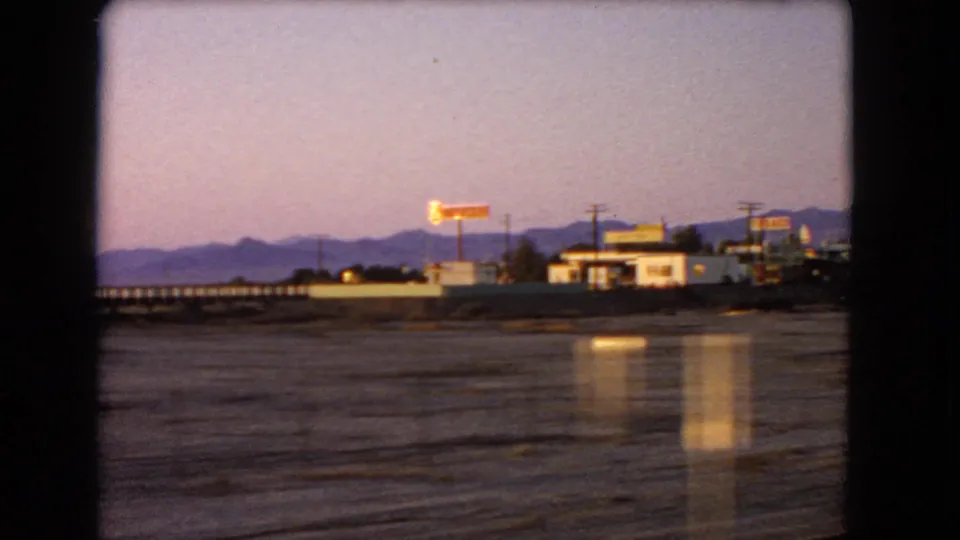 1966 Nevada 8mm frame with illuminated roadside signage, small-town buildings, utility poles, and desert mountains at twilight.