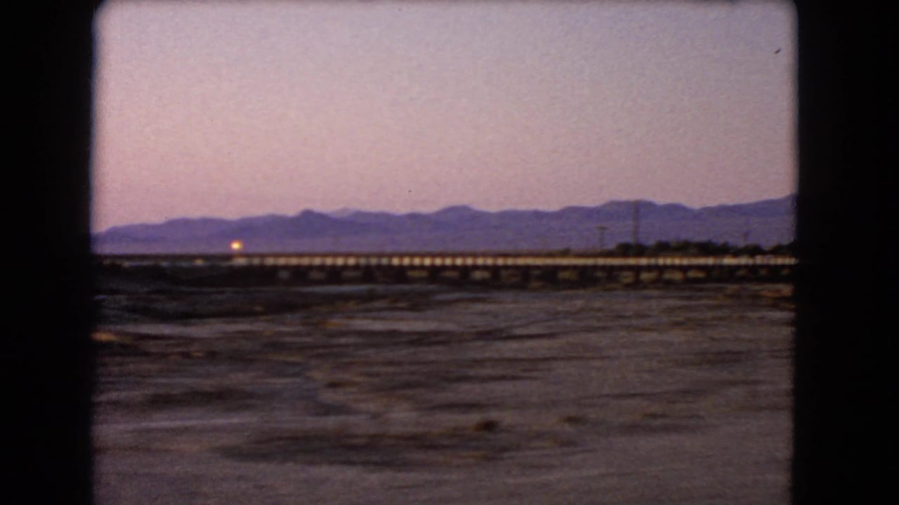 Long rail bridge and distant mountains seen through a dark vehicle or film-frame border.