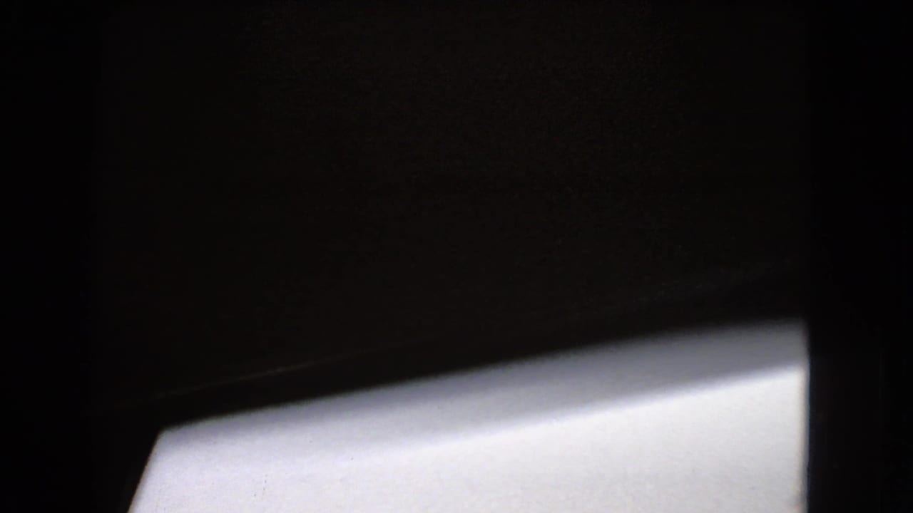 Dark framed 8mm view from inside or beside a moving vehicle, with a bright window or body panel occupying the lower portion.