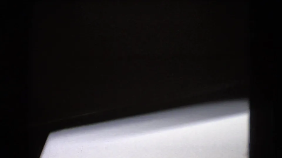 Dark framed 8mm view from inside or beside a moving vehicle, with a bright window or body panel occupying the lower portion.