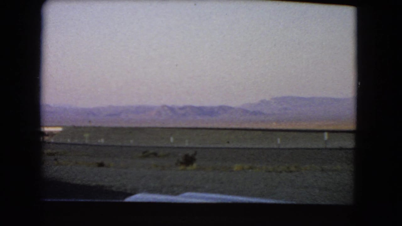 Open desert and low mountains visible beyond a roadside strip from a window.