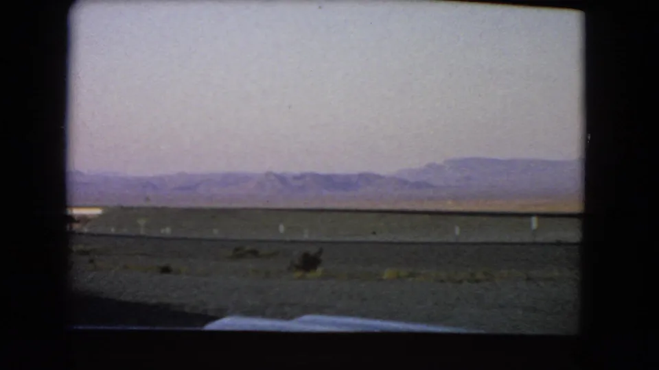 A moving-window view across Nevada desert terrain toward low purple hills under a pale sky.