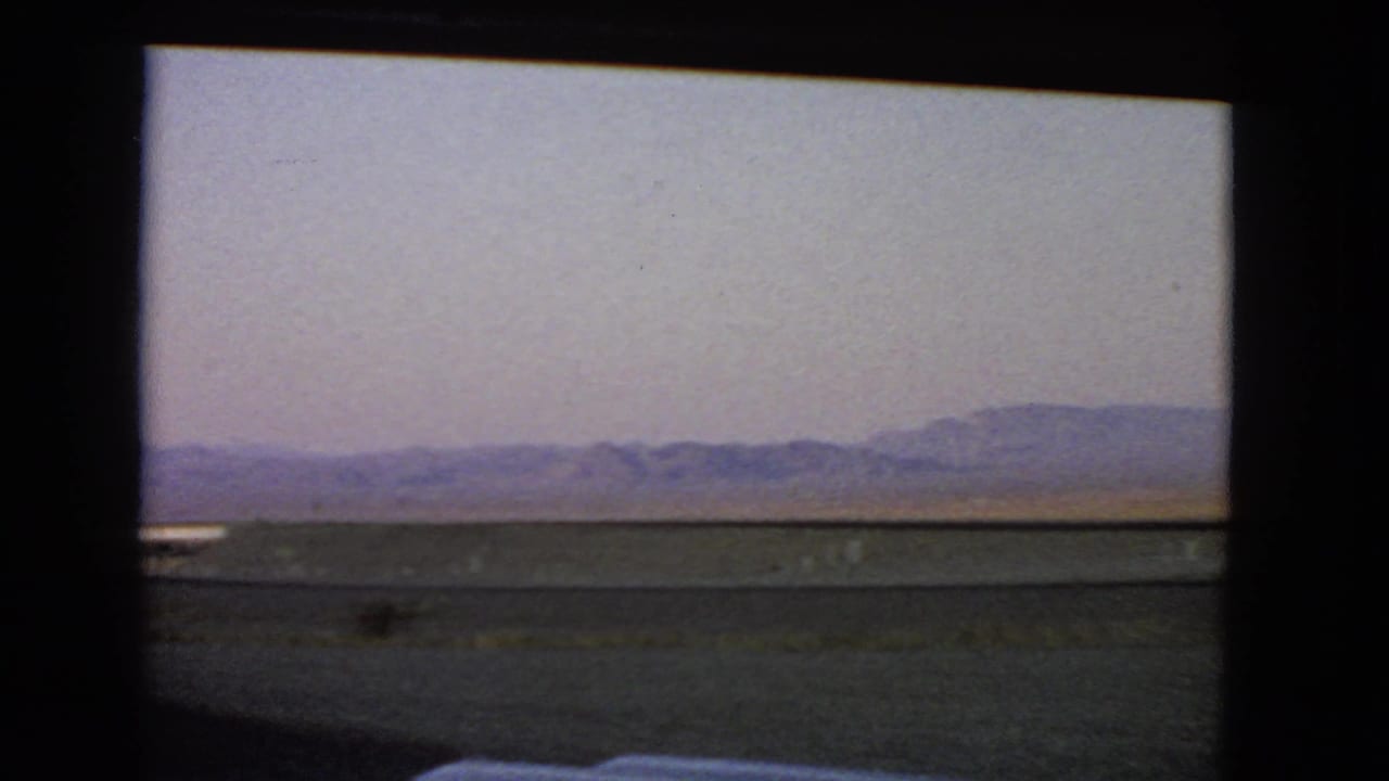 Nevada desert horizon and low hills appear through a vehicle window in soft 8mm color.