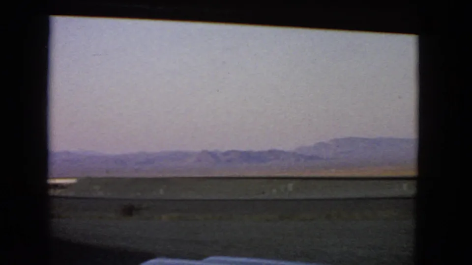 Nevada desert horizon and low hills appear through a vehicle window in soft 8mm color.