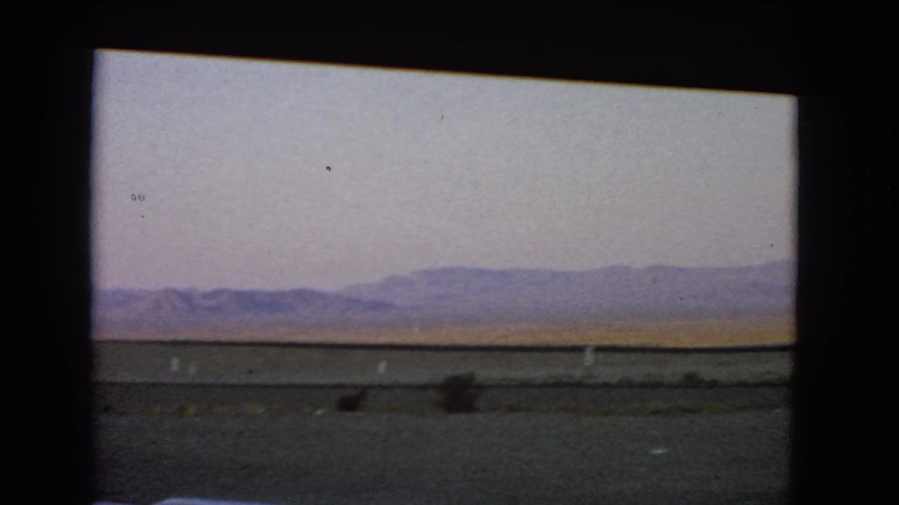 Final frame of the 1966 Nevada moving-vehicle view, showing sparse desert brush and hills beyond the roadside.