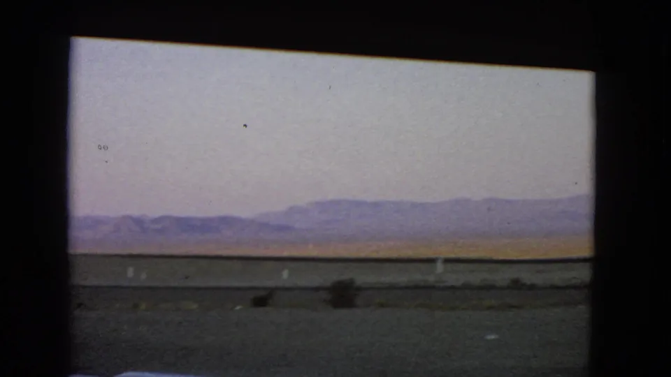 Final frame of the 1966 Nevada moving-vehicle view, showing sparse desert brush and hills beyond the roadside.