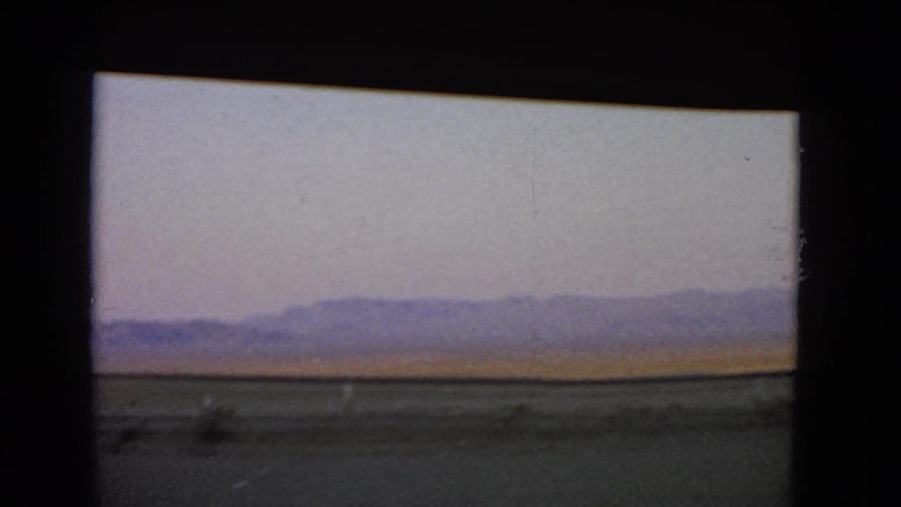 1966 Nevada 8mm view of open desert and a low purple mountain range beyond a roadside strip.
