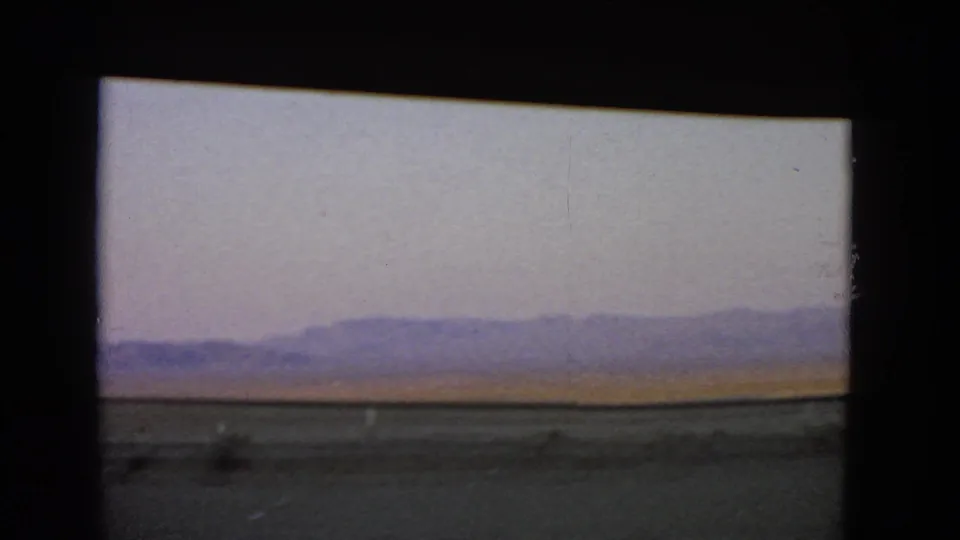 1966 Nevada 8mm view of open desert and a low purple mountain range beyond a roadside strip.