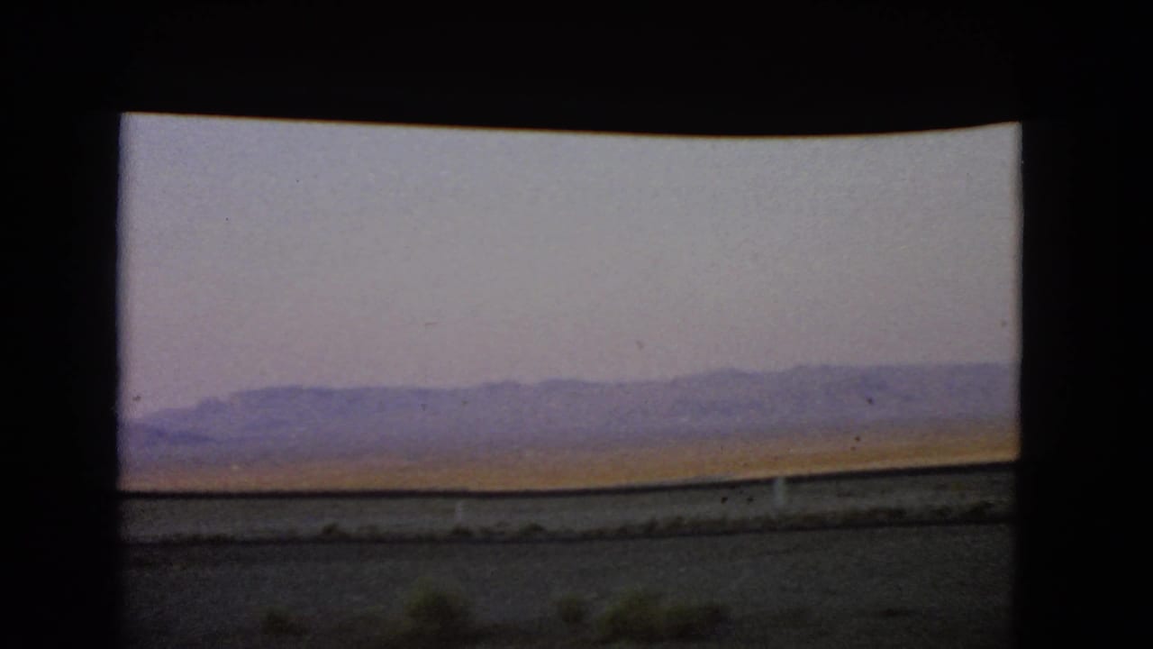 The Nevada desert landscape continues, with low mountains on the horizon and muted 8mm color.