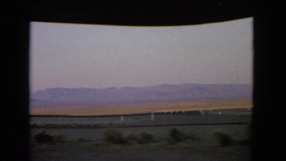 1966 Nevada desert landscape viewed through a moving car window, with roadside posts and hazy mountains beyond the plain.
