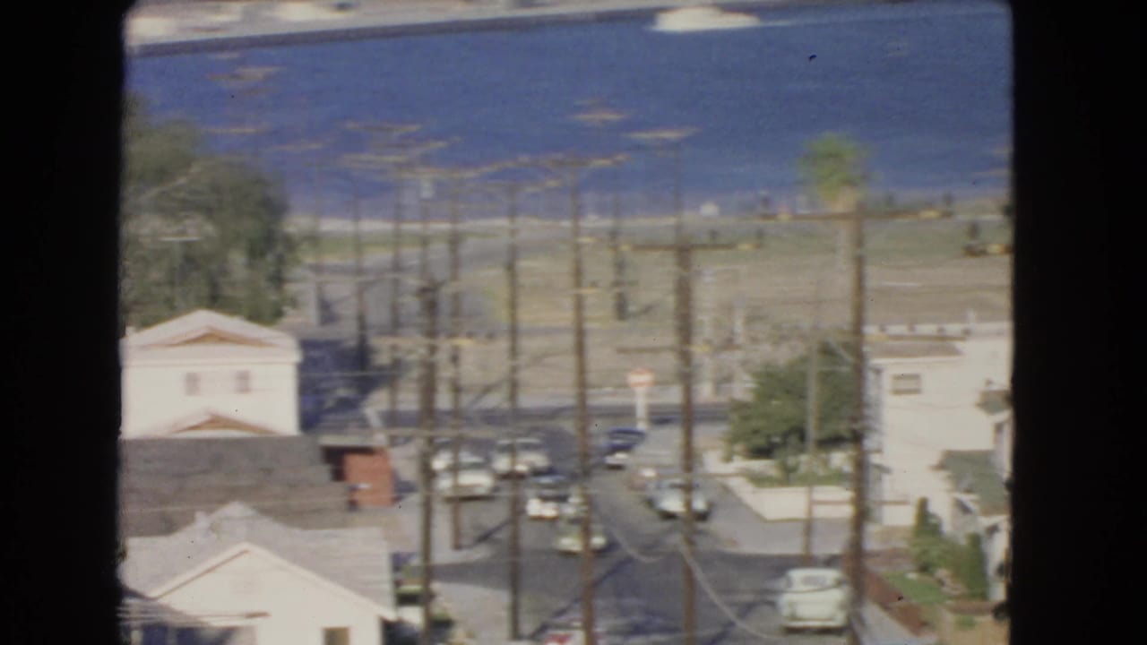 1966 San Pedro home-movie view looking over residential streets, utility poles, palm trees, cars, and blue harbor water.