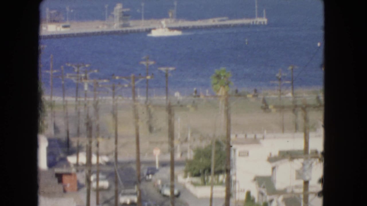 1966 San Pedro waterfront view with blue harbor water, distant pier or vessel, shoreline, utility poles, and residential foreground.
