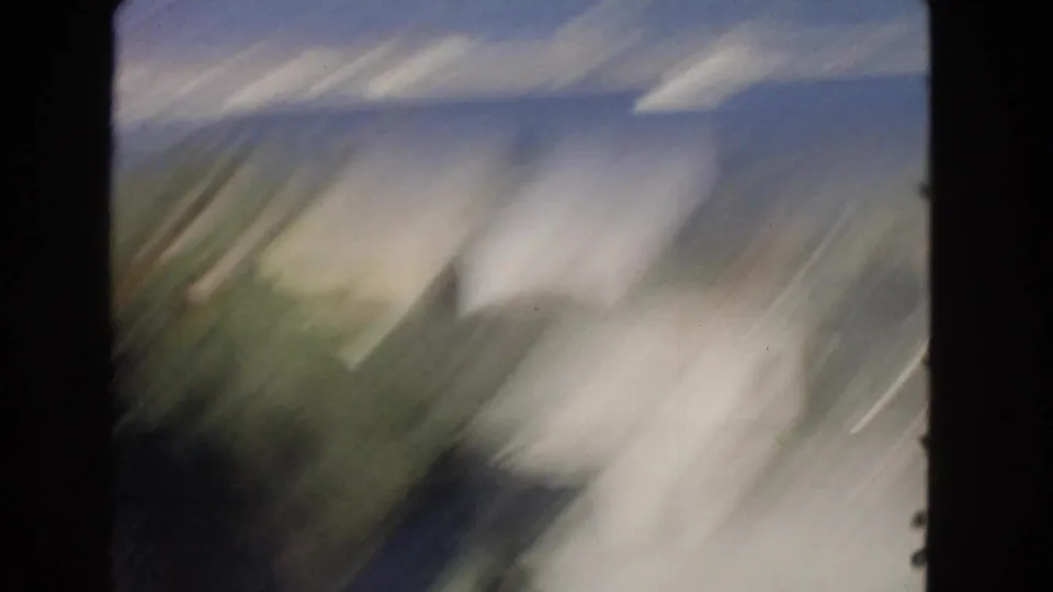 Blurred handheld 8mm movement over a San Pedro street area with pale buildings, road surface, and indistinct foreground shapes.