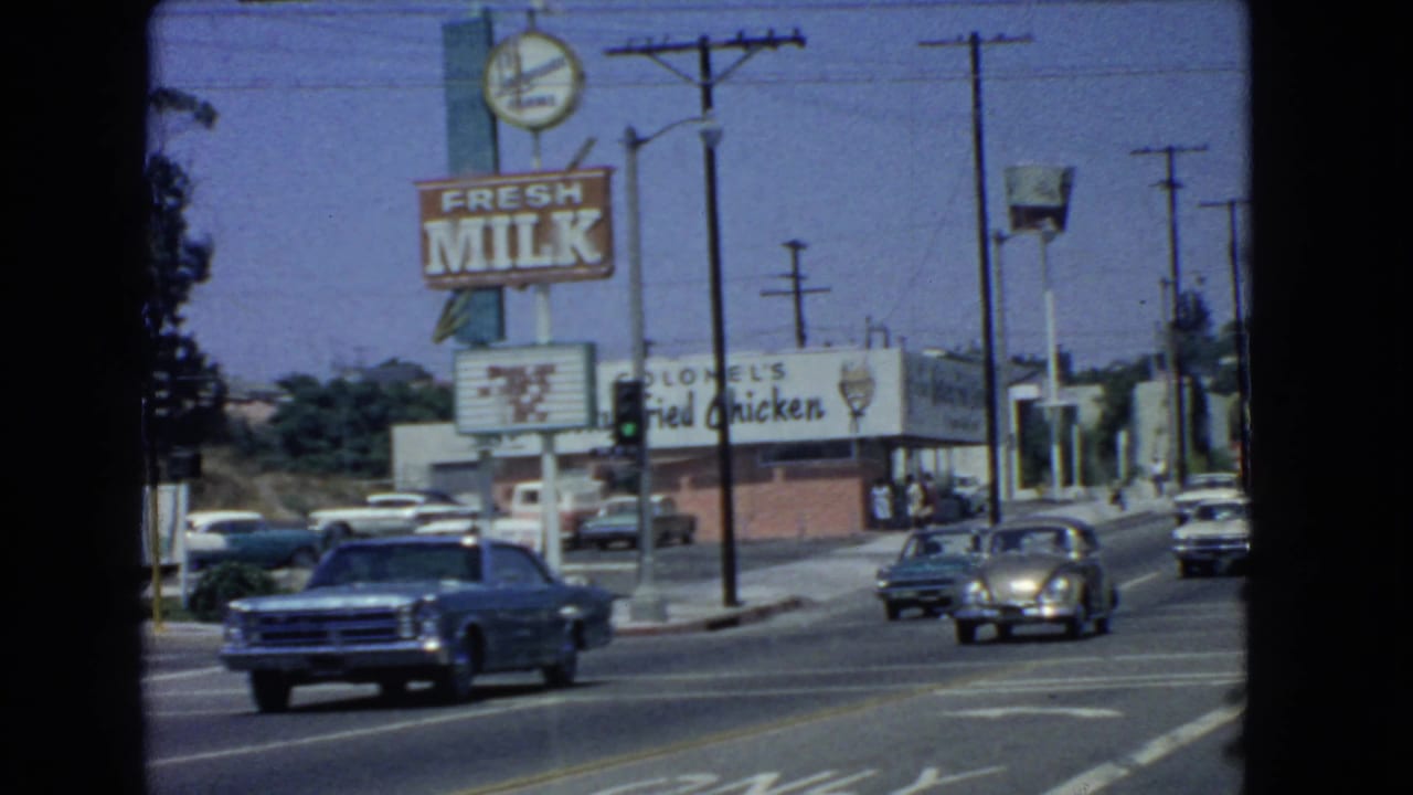 Cars drive past a roadside restaurant with Fresh Milk and fried chicken signs.