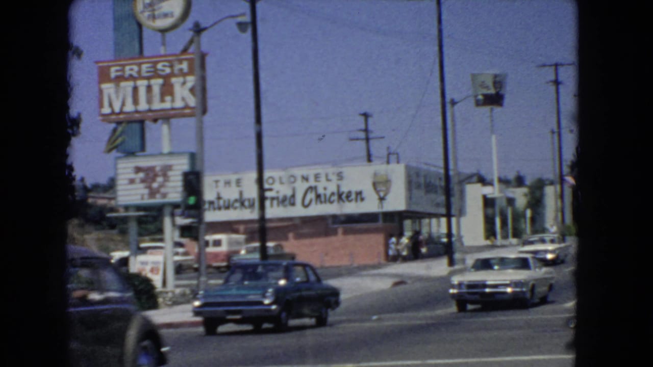 Late-clip view of the 1966 San Pedro intersection, showing cars, Fresh Milk signage, Colonel's Kentucky Fried Chicken branding, and distant pedestrians.