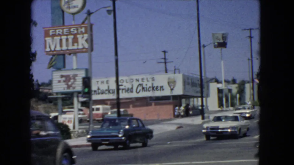 Late-clip view of the 1966 San Pedro intersection, showing cars, Fresh Milk signage, Colonel's Kentucky Fried Chicken branding, and distant pedestrians.