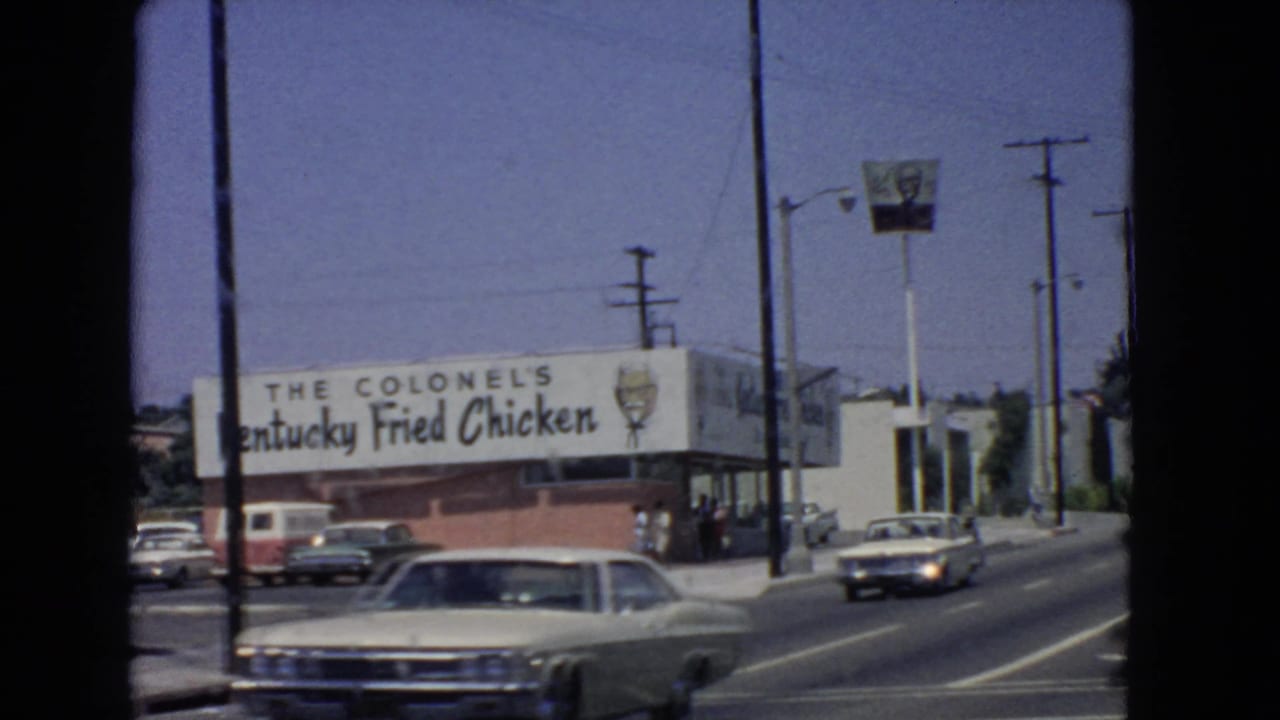 Kentucky Fried Chicken restaurant frontage with cars and pedestrians nearby.
