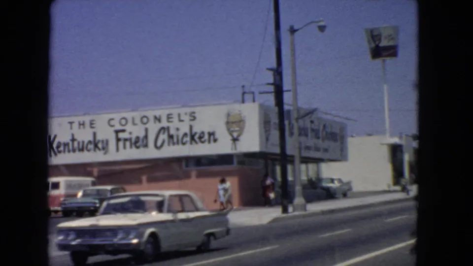 1966 San Pedro street view passing a Kentucky Fried Chicken storefront with Colonel signage, period cars, and pedestrians.