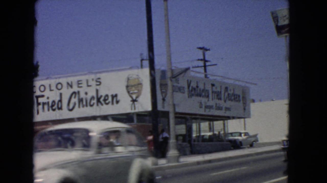 A fast-moving 1966 San Pedro street frame shows a blurred car crossing the Kentucky Fried Chicken exterior.